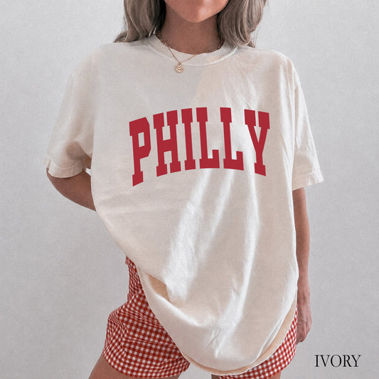 Woman wearing an ivory comfort colors t-shirt that says Philly on the front.