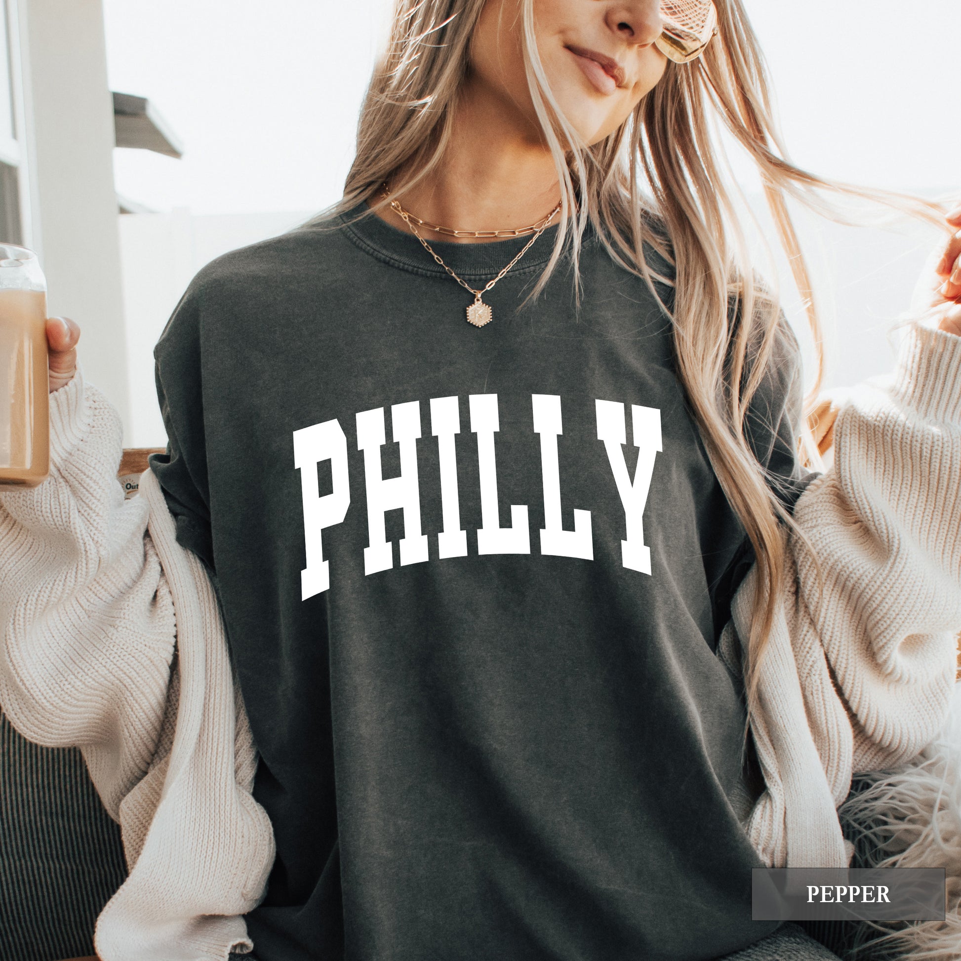 Woman wearing a pepper comfort colors t-shirt that says Philly on the front.