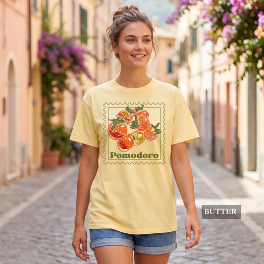Woman wearing a yellow t-shirt with 'Pomodoro' design on a street with flowers.