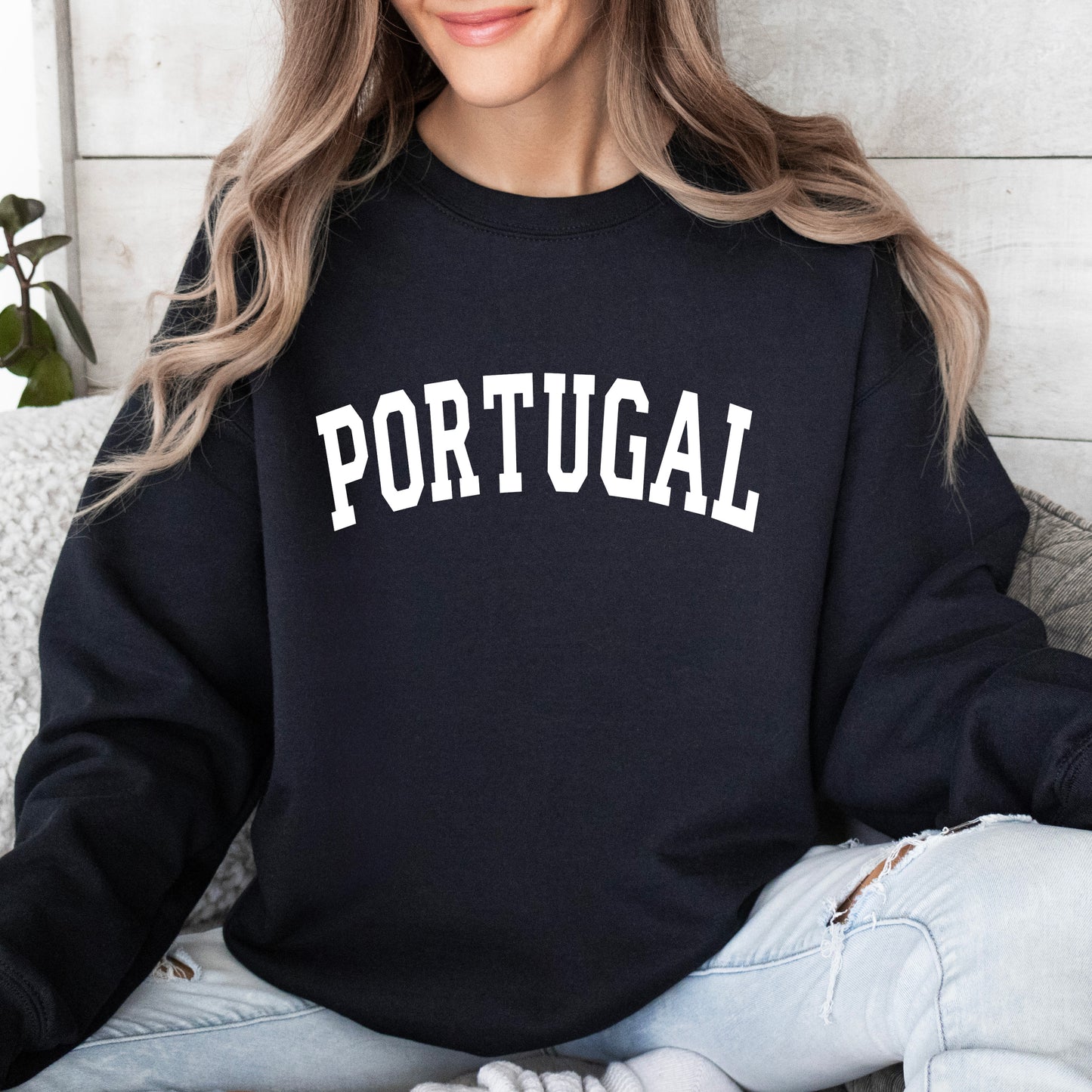 Person wearing a black sweatshirt with 'PORTUGAL' printed on it, sitting against a light wooden wall.