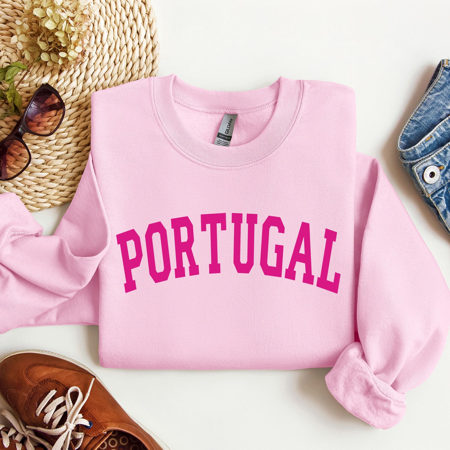 Pink sweatshirt with 'PORTUGAL' printed in pink on a white surface with accessories.