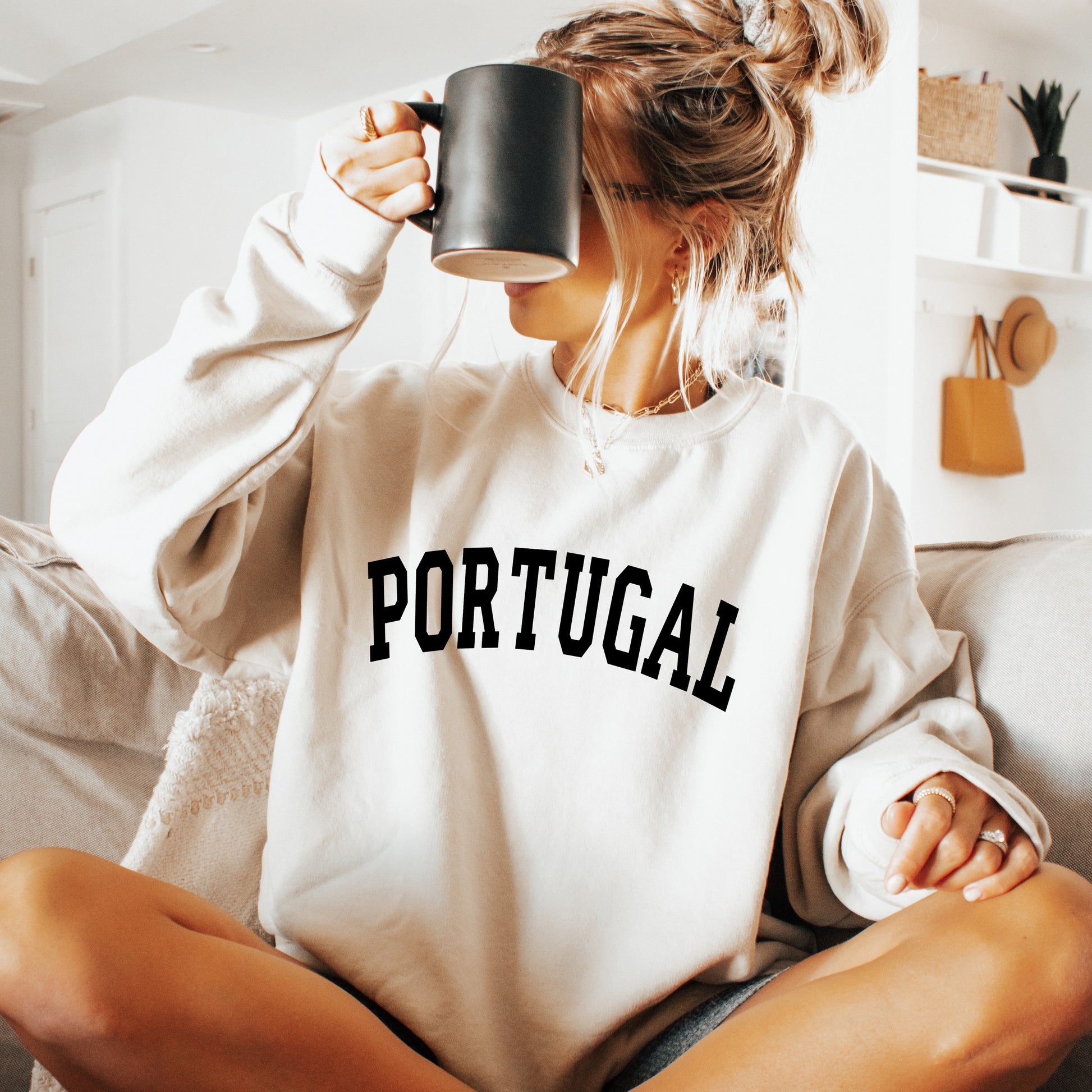 Person wearing a white sweatshirt with 'PORTUGAL' printed on it, holding a mug.
