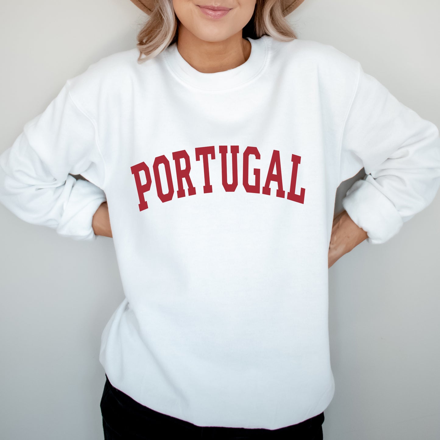Person wearing a white sweatshirt with 'PORTUGAL' printed in red on a plain background