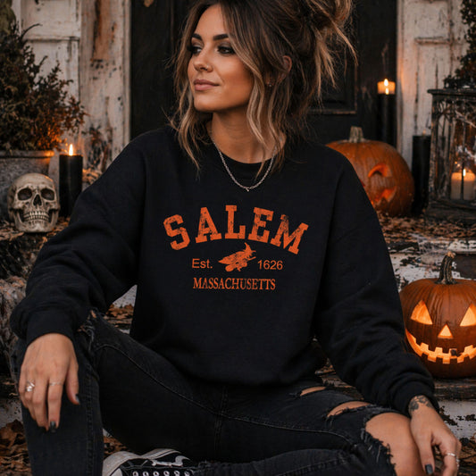Person wearing a black sweatshirt with 'Salem, Massachusetts' text in an autumnal setting with pumpkins and a skull.