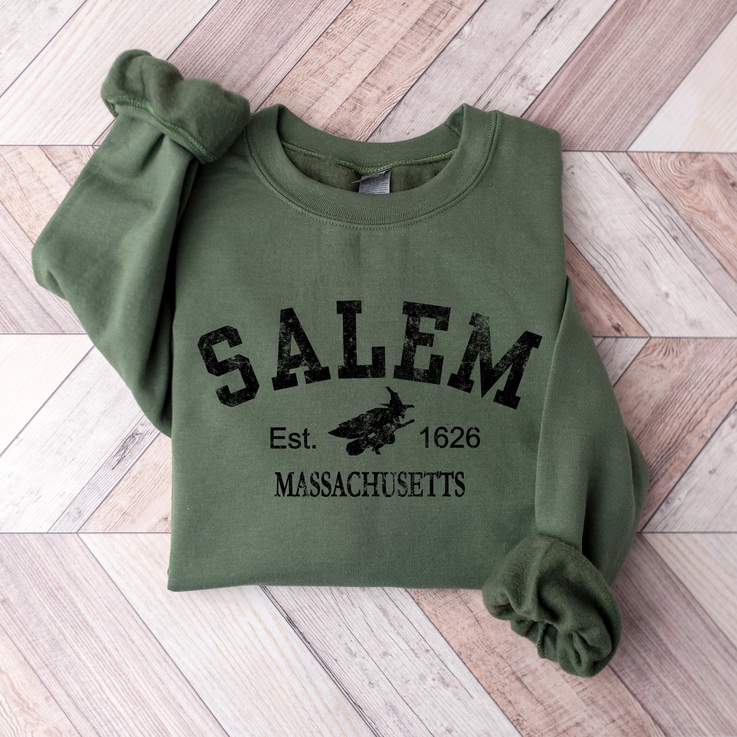 Green sweatshirt with 'Salem, Massachusetts' text on a wooden floor