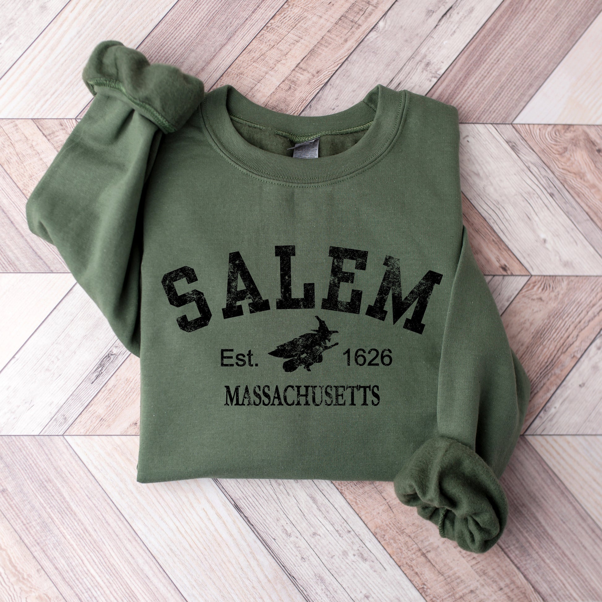 Green sweatshirt with 'Salem, Massachusetts' text on a wooden floor