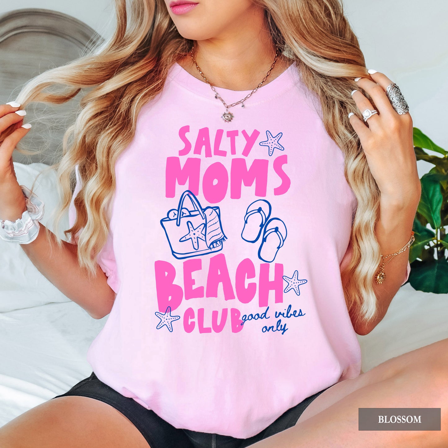 Person wearing a pink t-shirt with 'Salty Moms Beach Club' text and graphics.