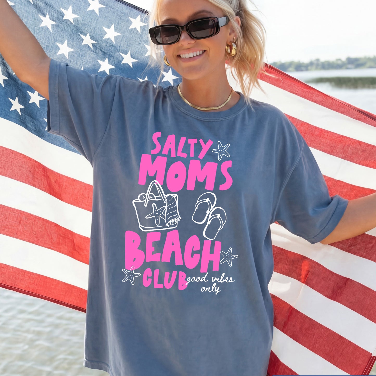Woman wearing a t-shirt with 'Salty Moms Beach Club' design in front of an American flag.