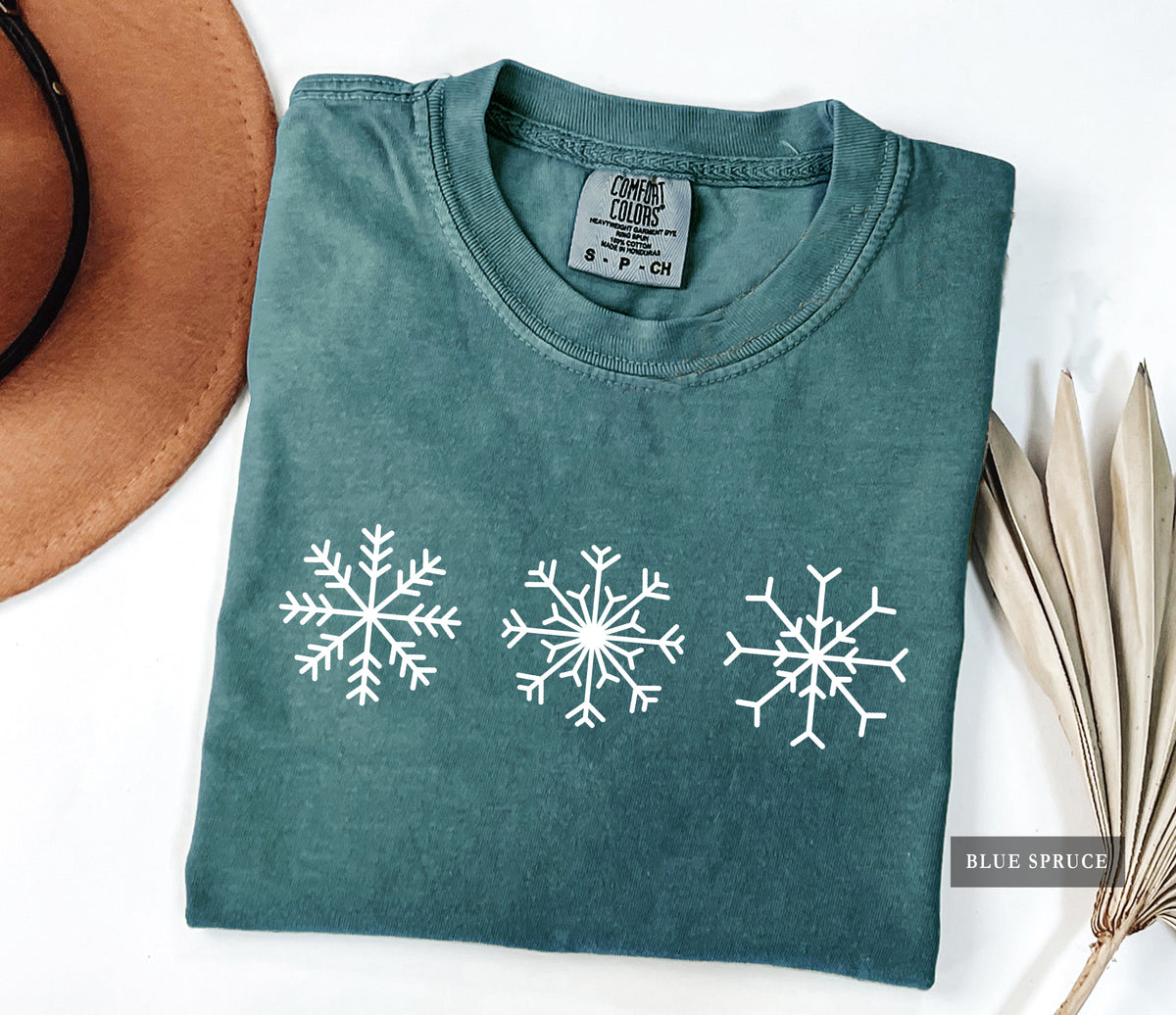 A blue spruce comfort colors t-shirt with three snowflakes on the front.