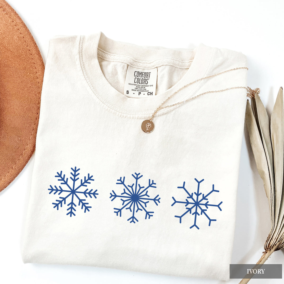 An ivory comfort colors t-shirt with three snowflakes on the front.