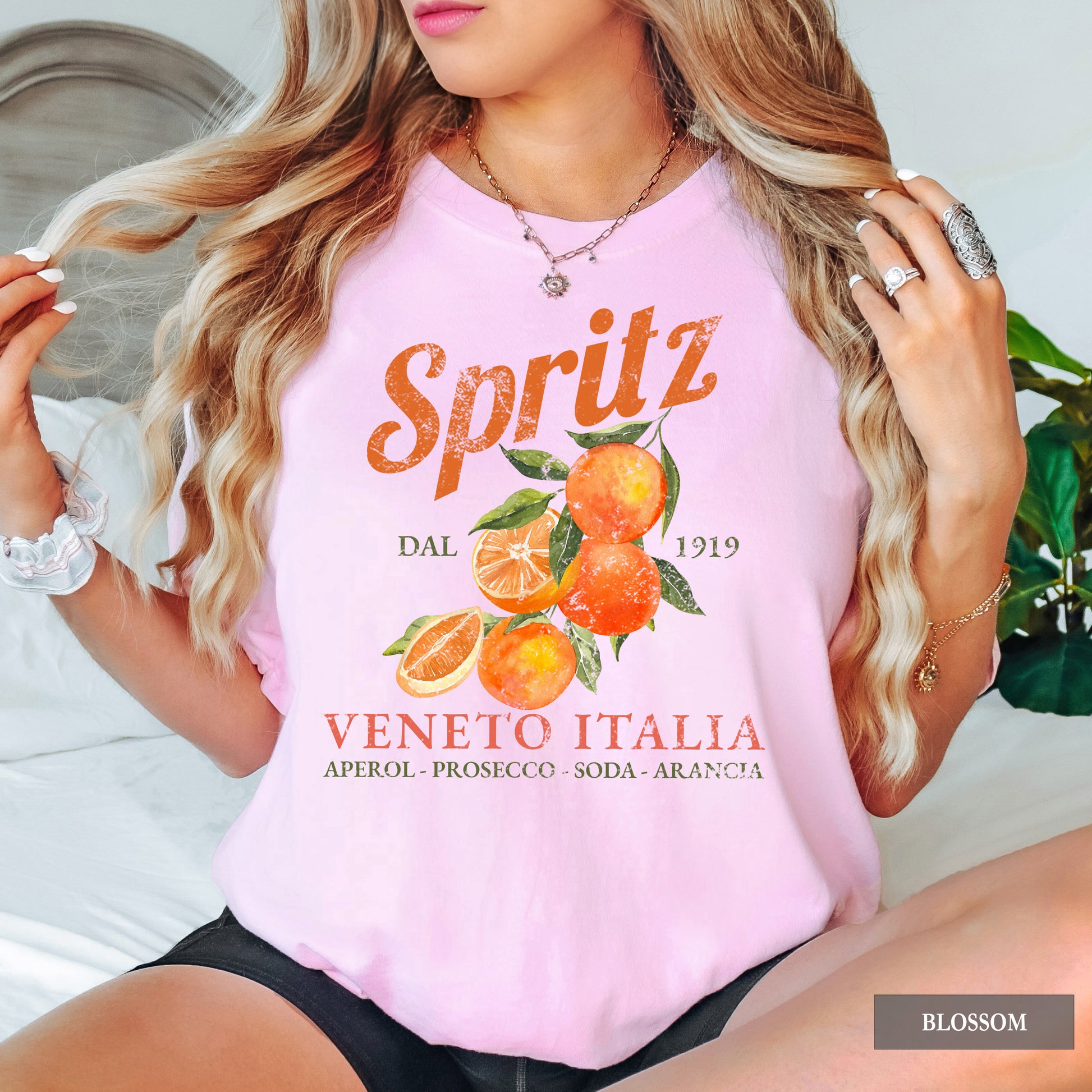 A woman wearing a pink t-shirt that says Spritz Veneto Italia and has oranges on it.