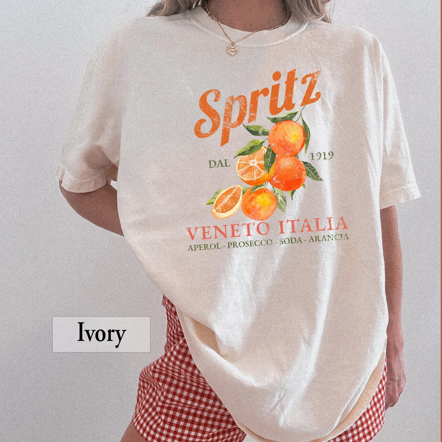 A woman wearing an ivory t-shirt that says Spritz Veneto Italia and has oranges on it.