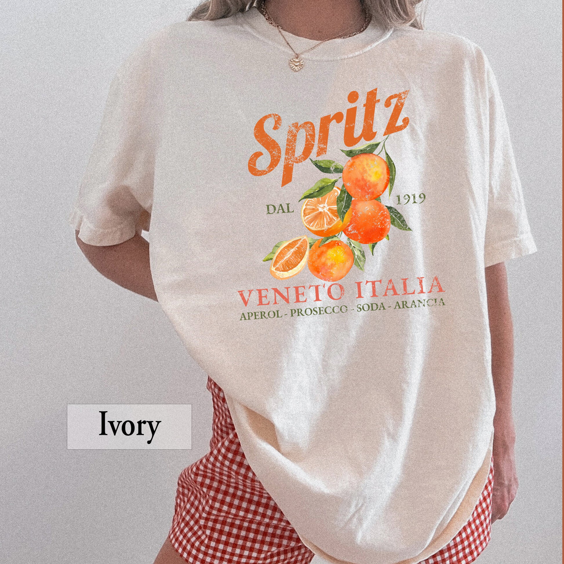 A woman wearing an ivory t-shirt that says Spritz Veneto Italia and has oranges on it.