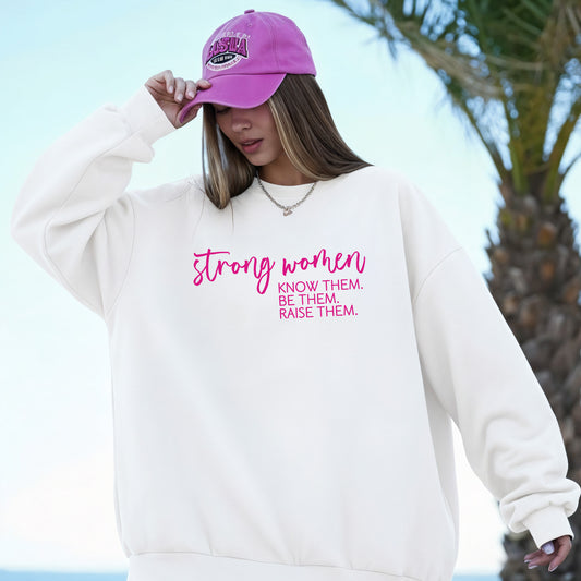 A woman wearing a white crewneck sweatshirt with the white printed text 'strong women KNOW THEM. BE THEM.