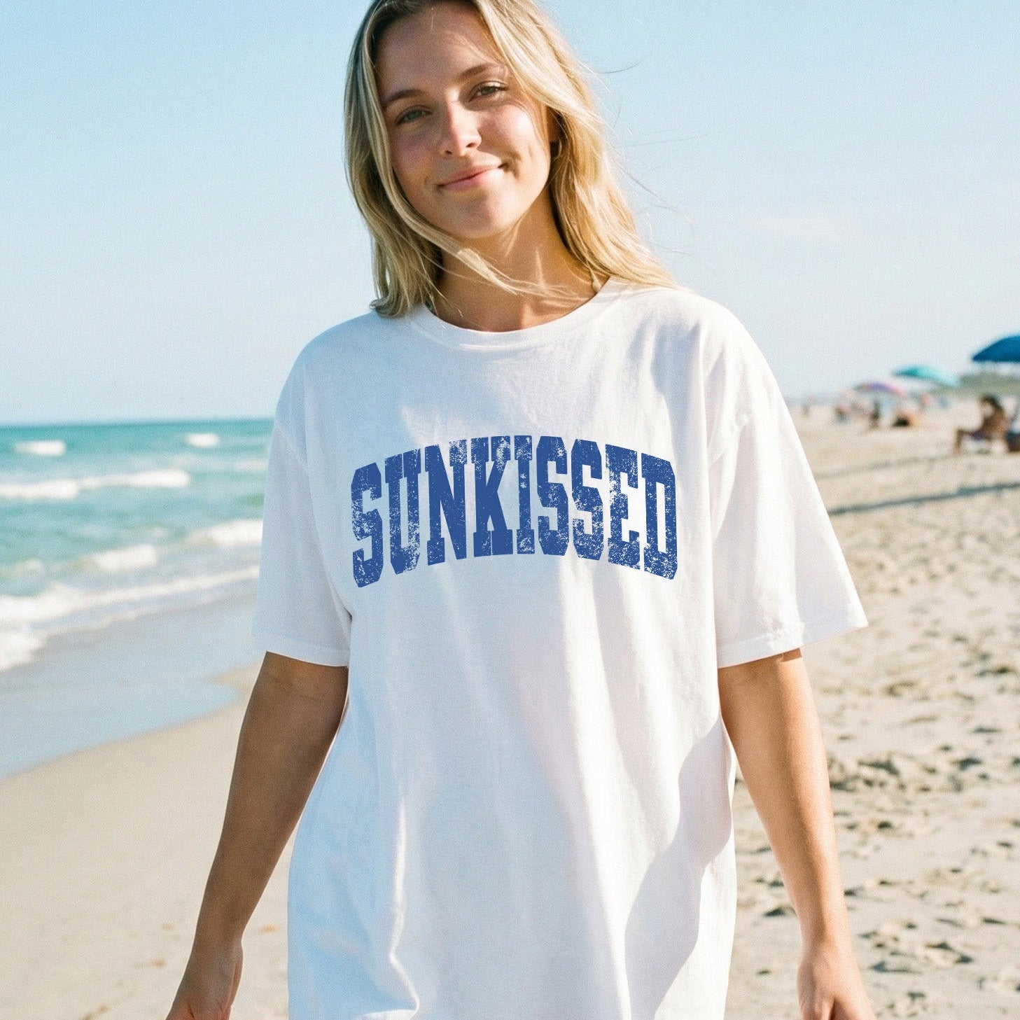 Woman wearing a white t-shirt with 'SUNKISSED' text on a beach