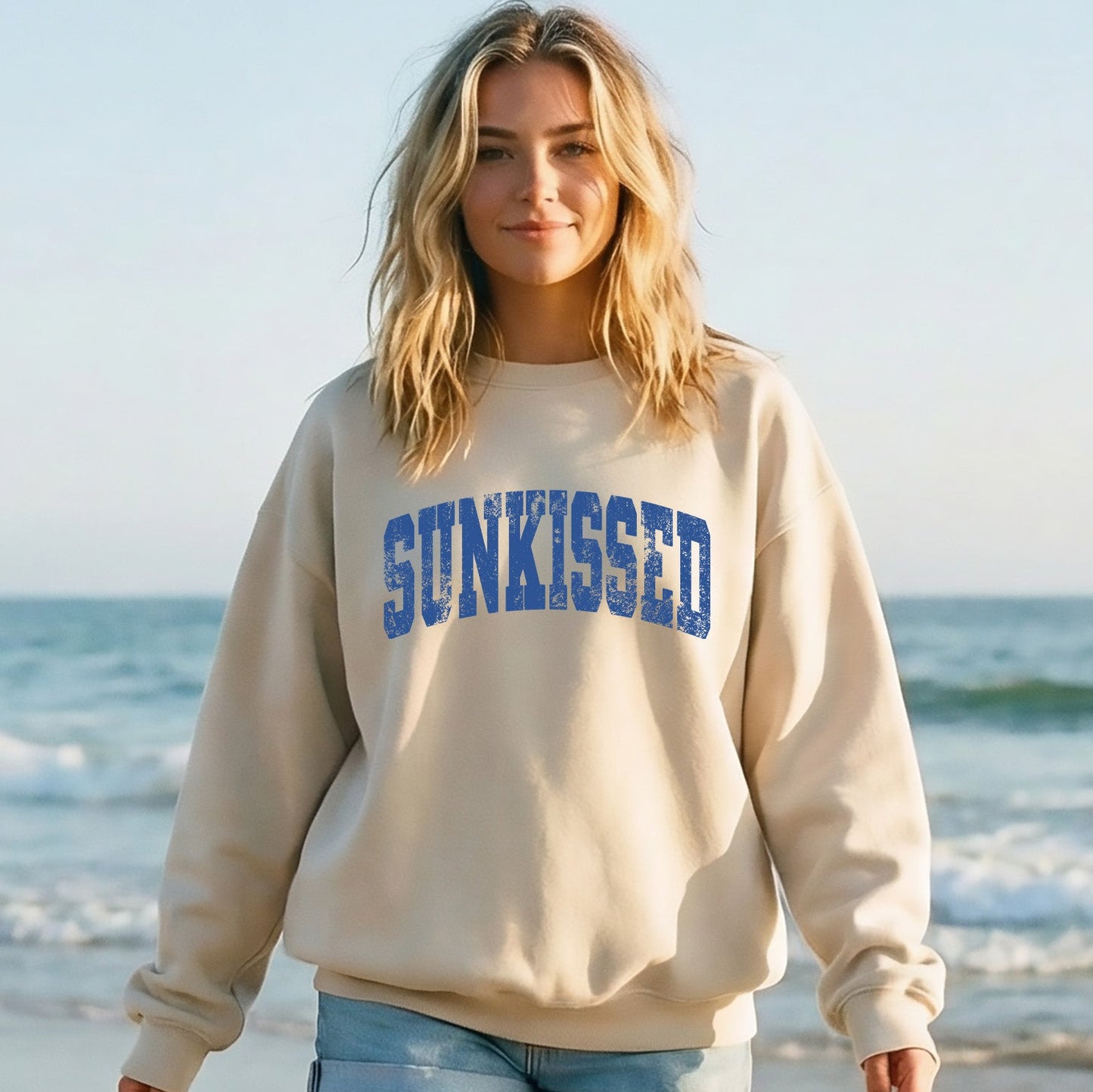 Woman wearing a beige sweatshirt with 'SUNKISSED' text on a beach