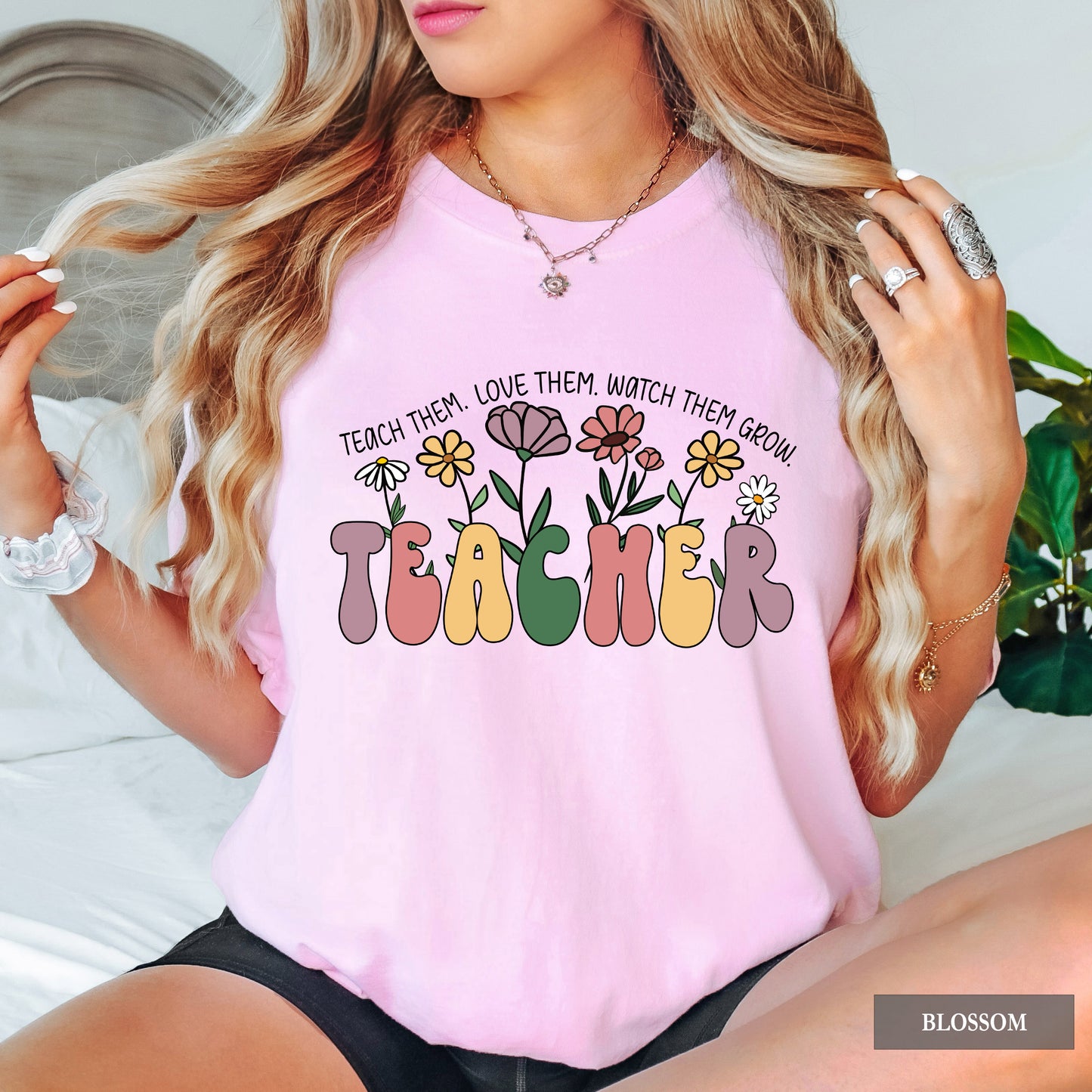 Person wearing a pink t-shirt with a colorful 'TEACHER' design and floral elements.