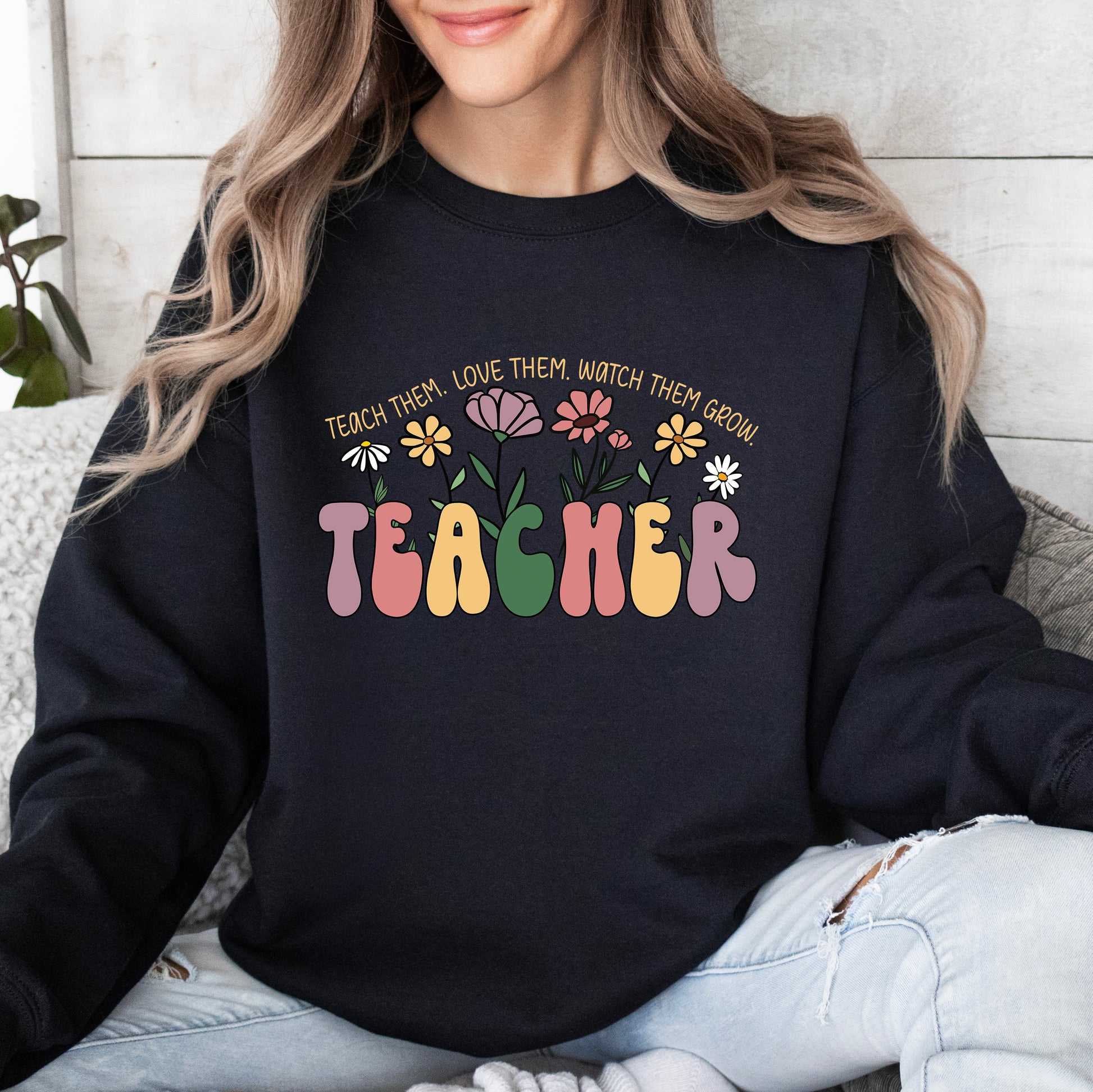 Person wearing a black sweatshirt with colorful 'TEACHER' text and floral design.