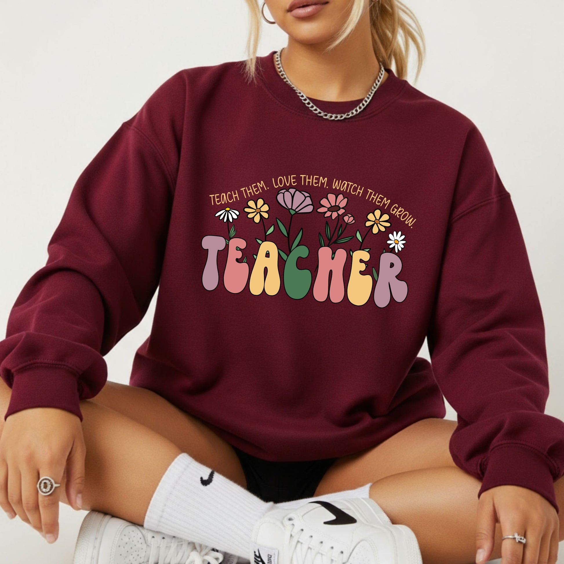 Maroon sweatshirt with colorful text and floral design, worn by a person sitting on the floor.