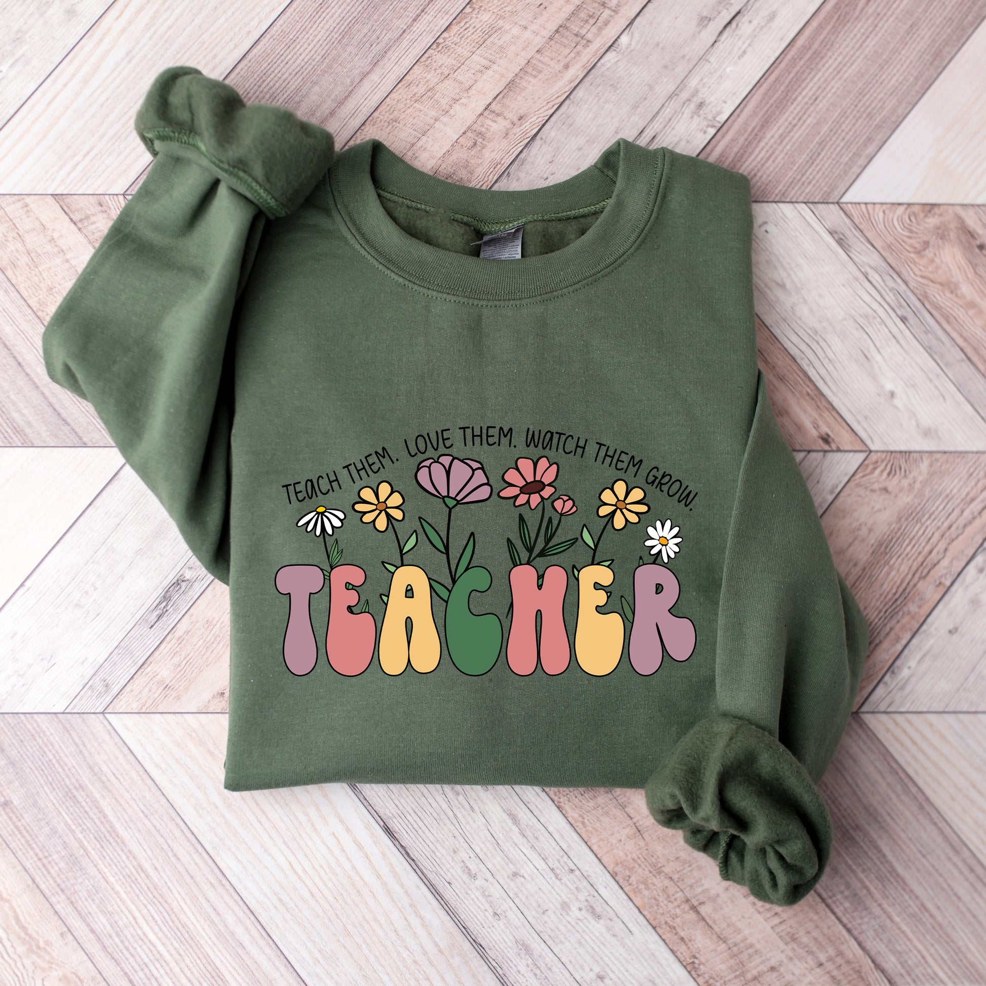 Green sweatshirt with colorful 'TEACHER' text and floral design on a wooden floor.