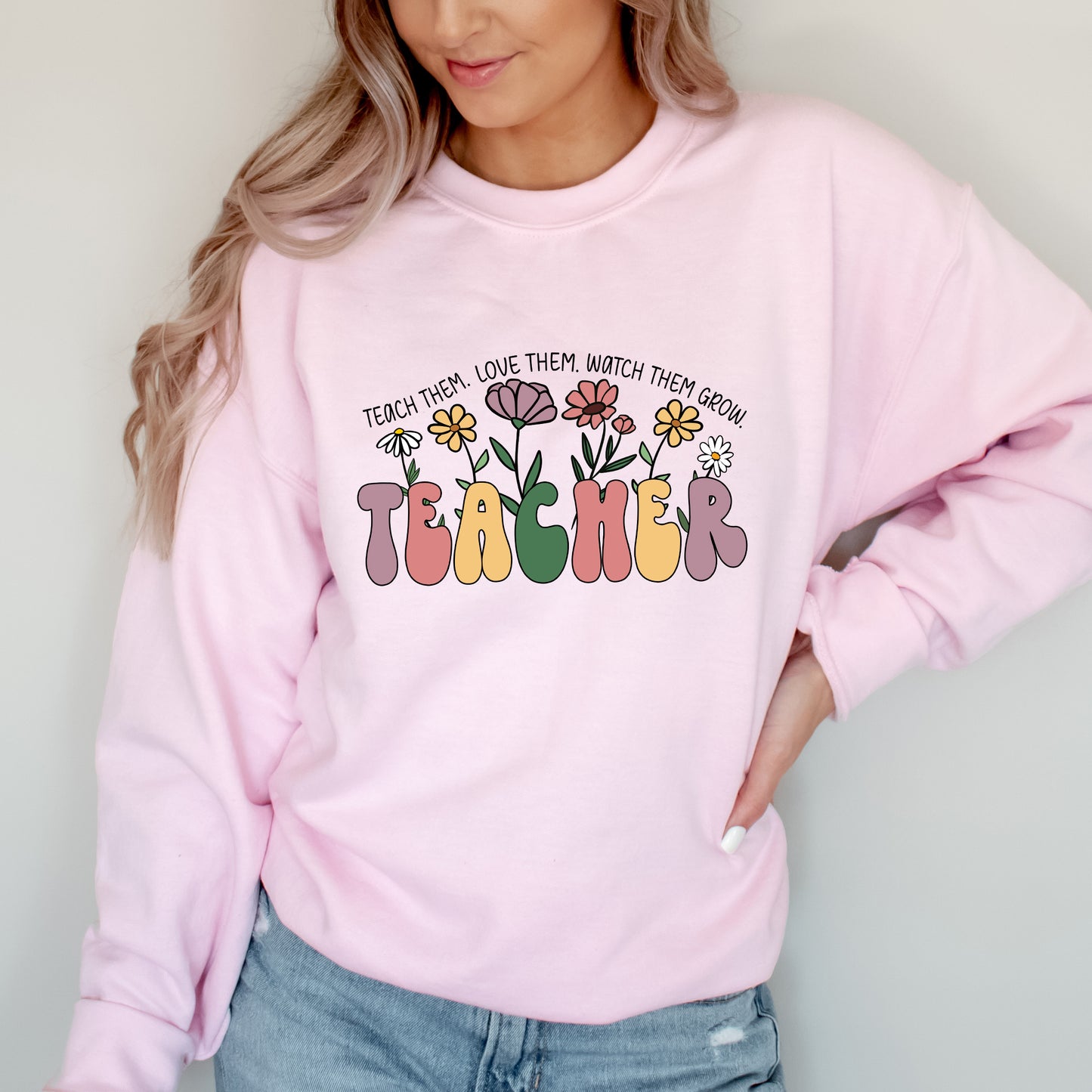 Person wearing a pink sweatshirt with 'TEACHER' and floral design text.