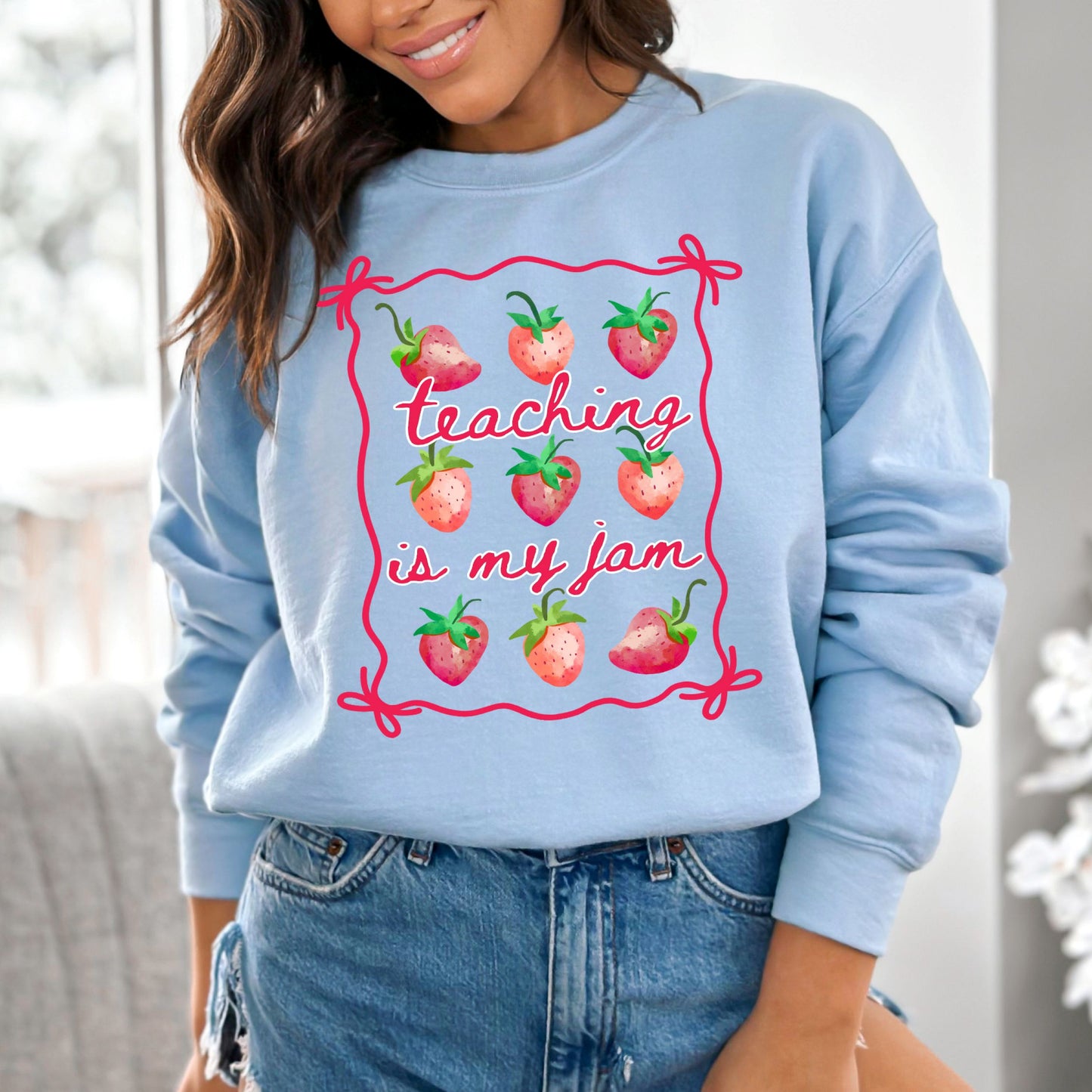 Light blue sweatshirt with strawberry design and text 'Teaching is my jam' worn by a person.