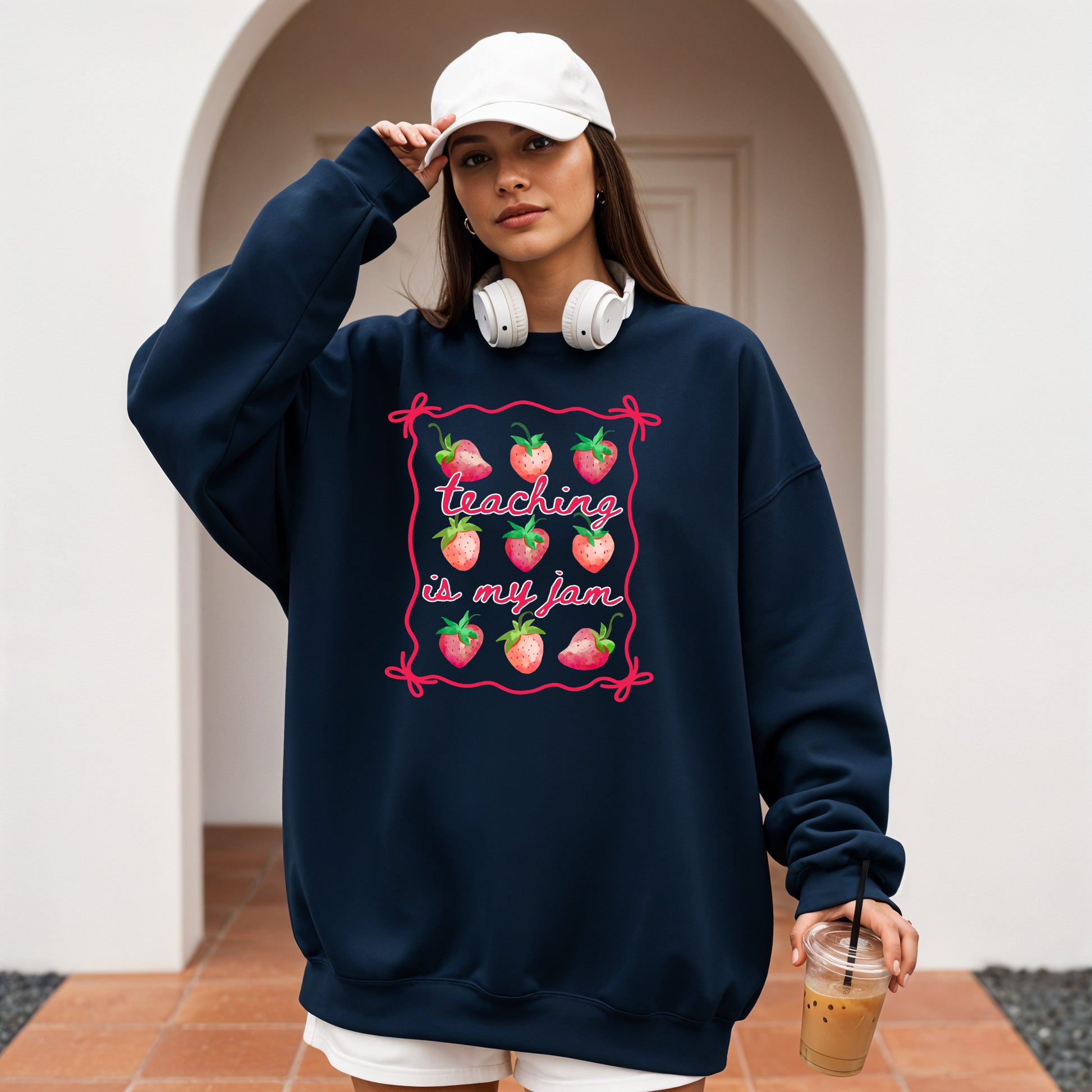Person wearing a navy sweatshirt with a strawberry design and text, holding a drink.