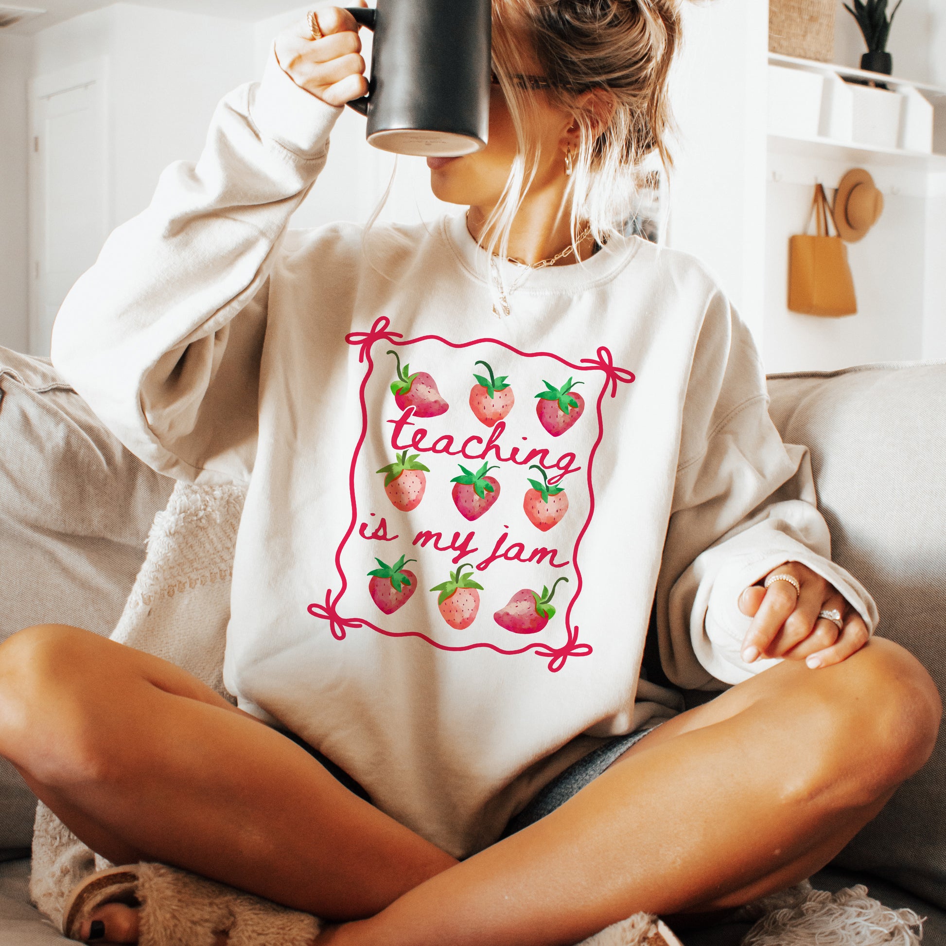 Person wearing a white hoodie with 'Teaching is my jam' design, sitting on a couch.