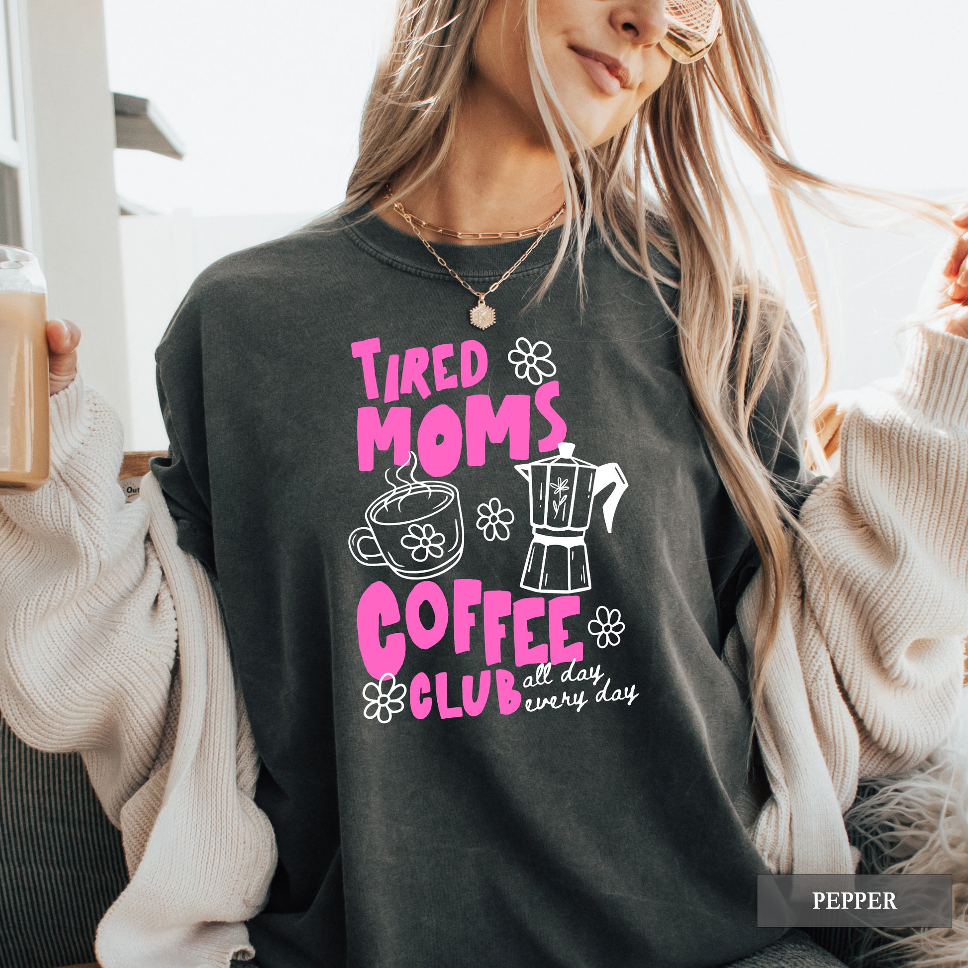 Person wearing a black sweatshirt with pink and white text and graphics, holding a drink.