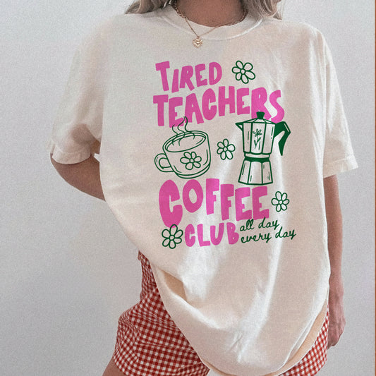 Person wearing a white t-shirt with 'Tired Teachers Coffee Club' design on a plain background
