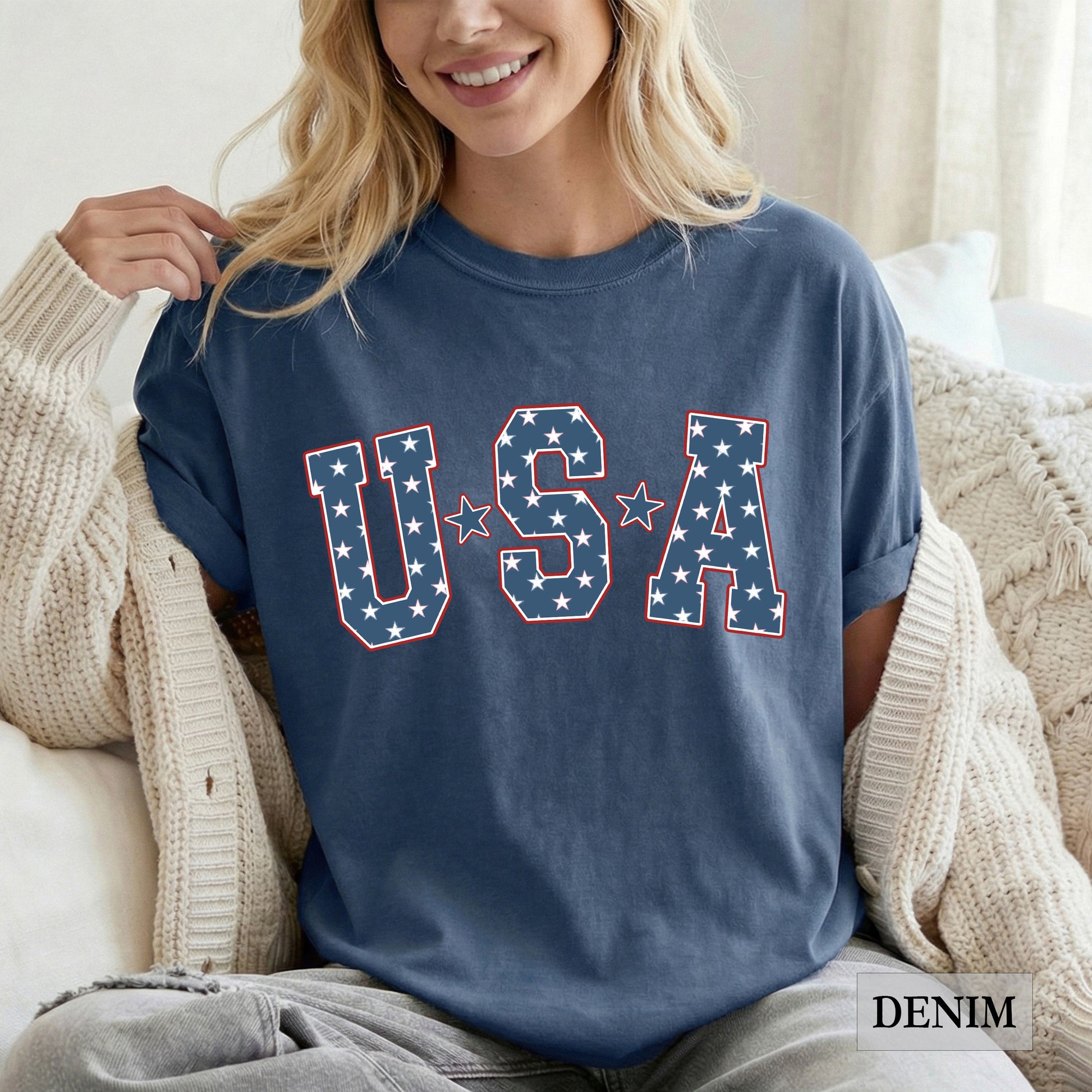 Woman wearing a blue 'USA' t-shirt with star design, sitting on a couch.