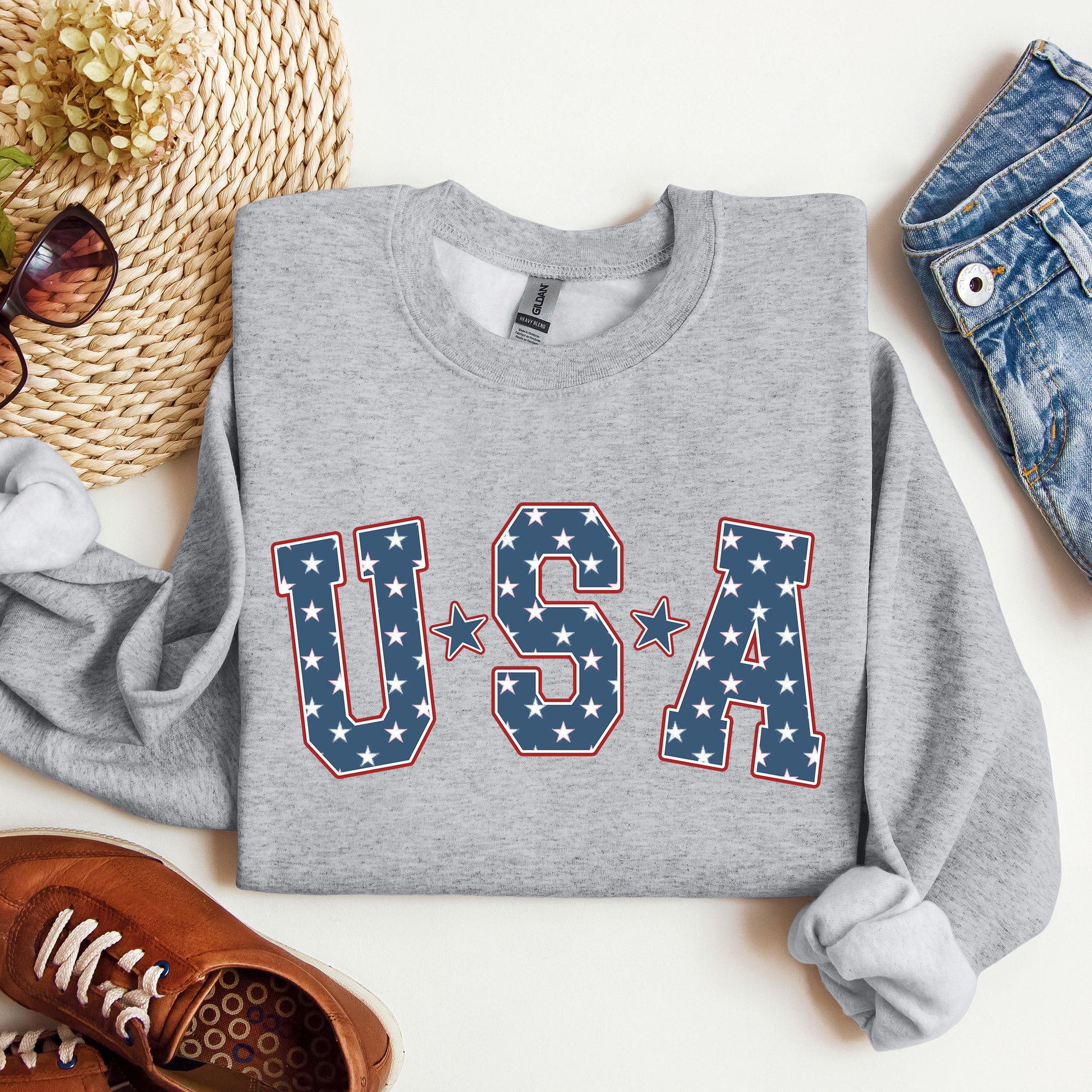 Gray sweatshirt with 'USA' text on a white surface with accessories around