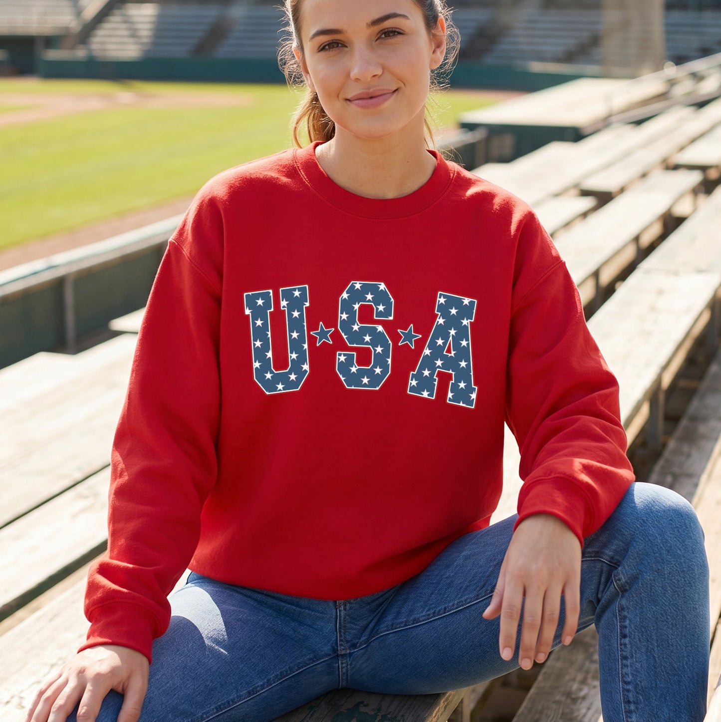 Woman wearing a red sweatshirt with 'U.S.A' printed on it, sitting in a stadium.
