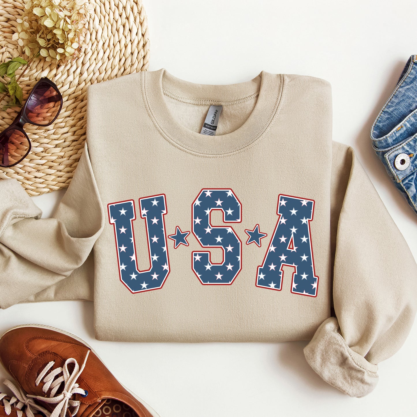Beige sweatshirt with 'U.S.A' print on a white surface with accessories.