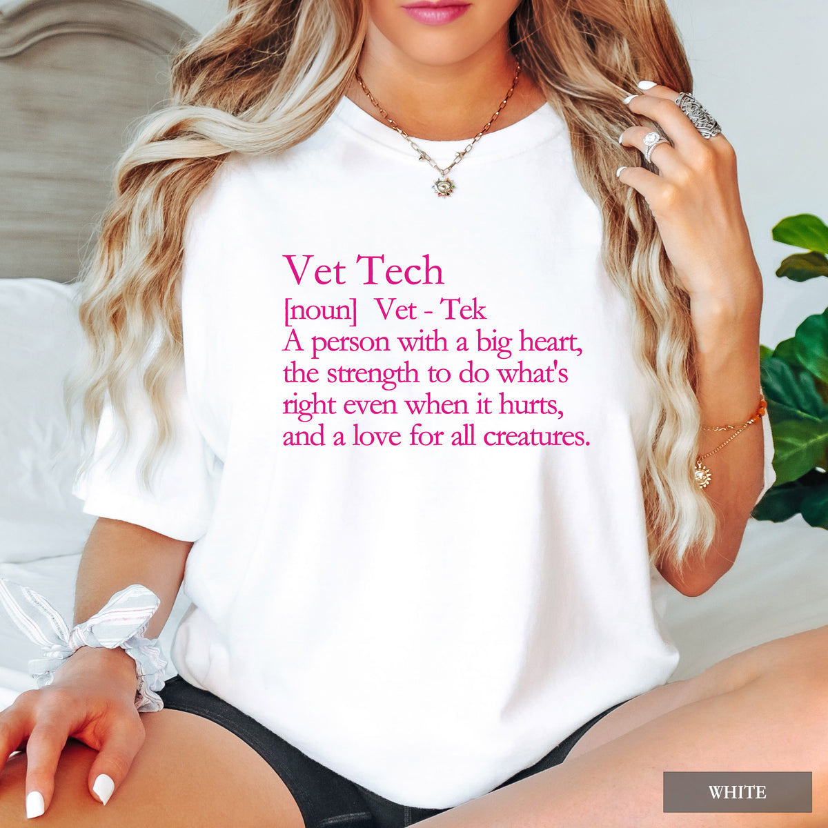 A woman wearing a white graphic T-shirt with pink text defining 'Vet Tech' in a humorous way. The photo is cropped from the mouth down, showing her blonde hair, jewelry, and black shorts, with a small 'WHITE' label in the bottom right corner.