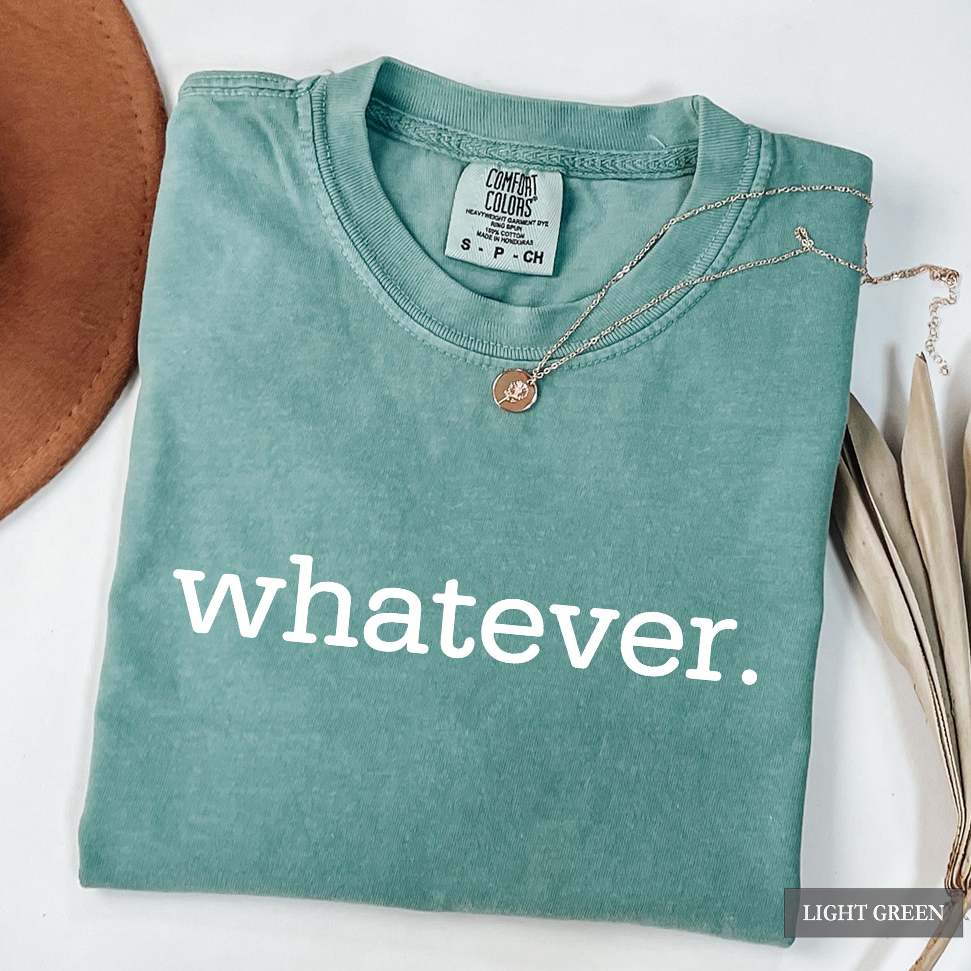 A folded light green t-shirt with the word 'whatever.' printed in white lowercase letters across the front.
