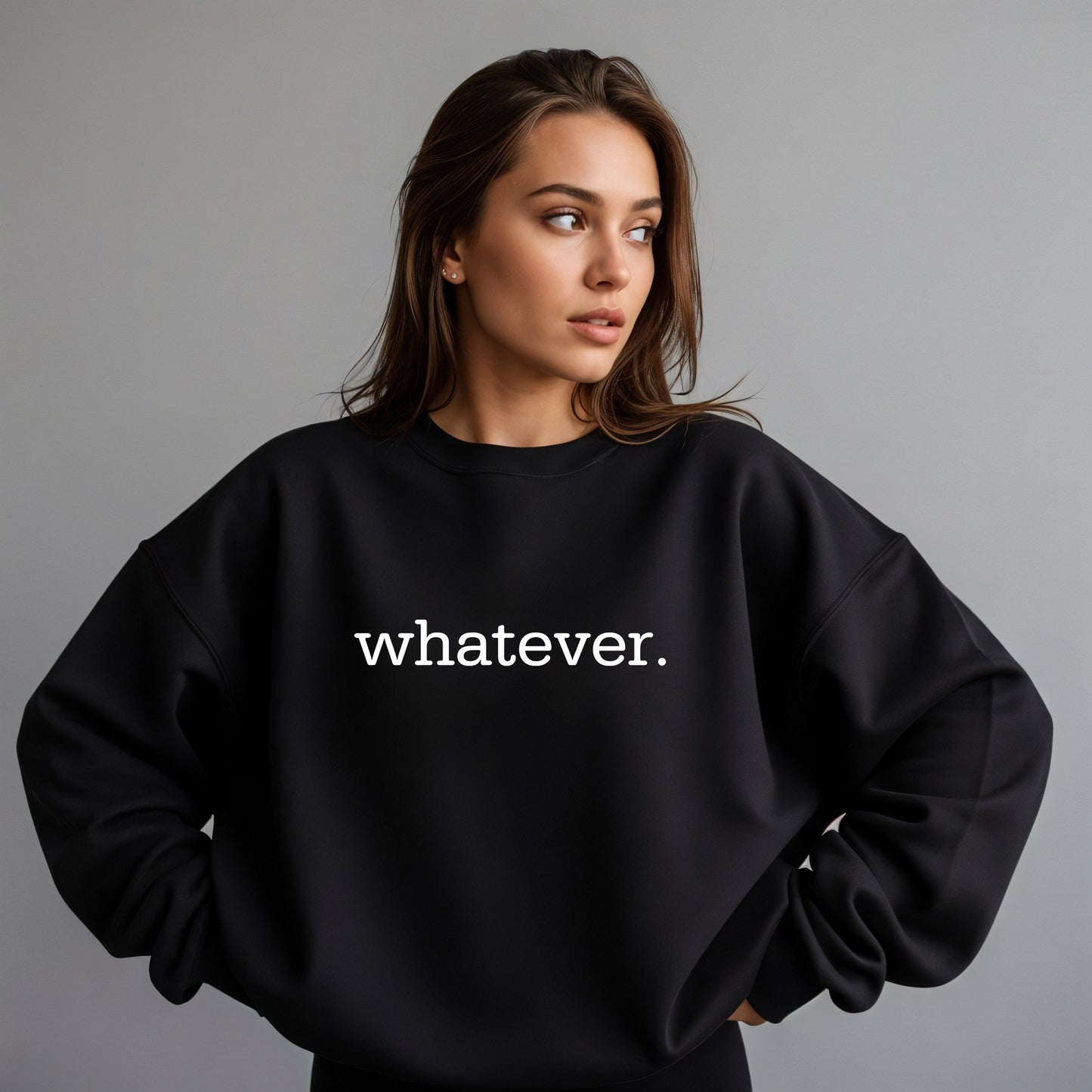 A woman wearing a black crewneck sweatshirt with the word 'whatever.' printed in white lowercase serif text across the chest, posed against a solid gray studio background.