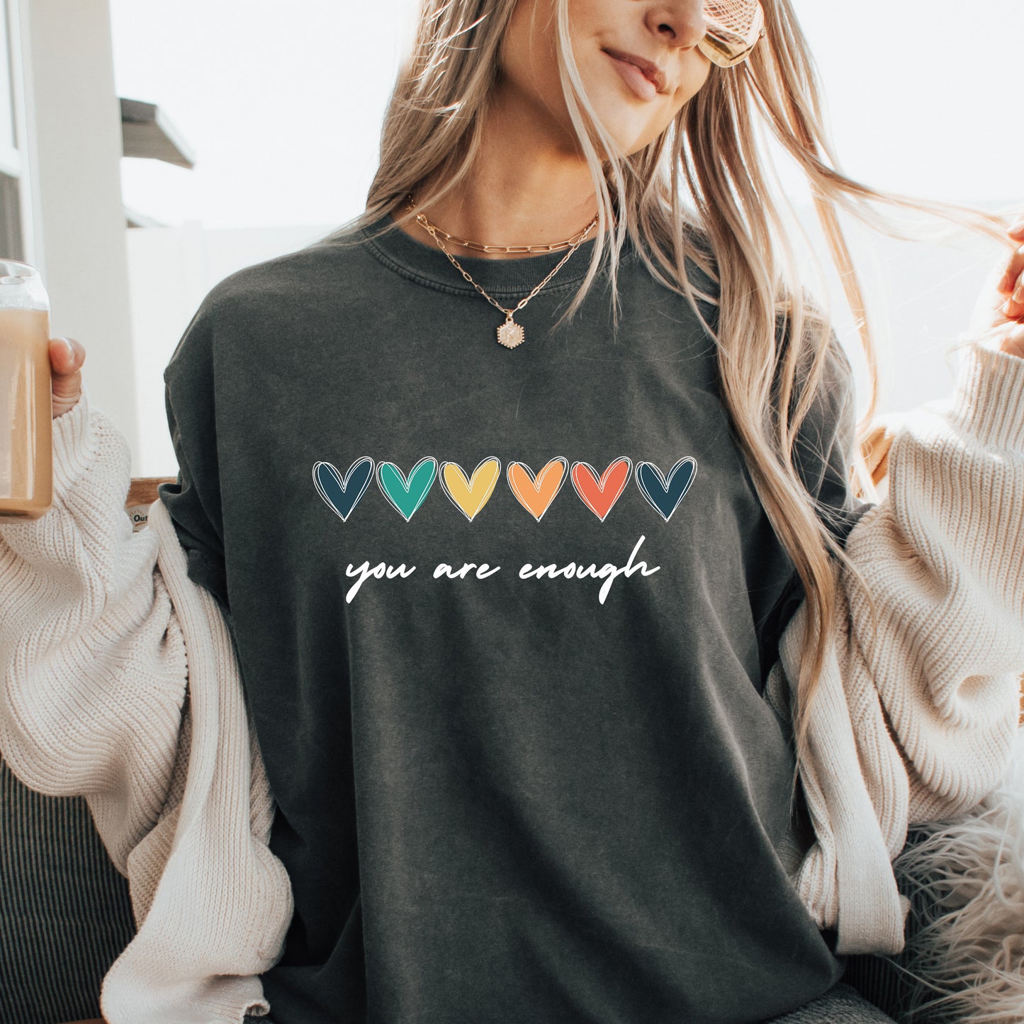 Person wearing a dark gray sweatshirt with colorful heart symbols and 'you are enough' text.