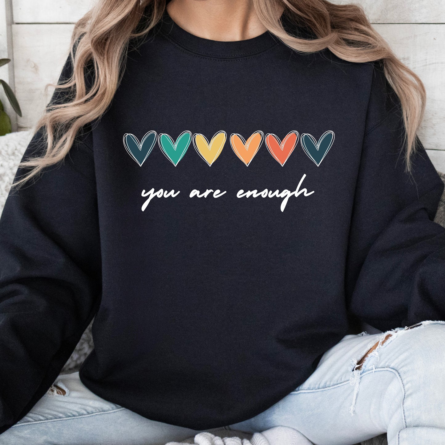 Person wearing a black sweatshirt with colorful heart designs and 'you are enough' text.