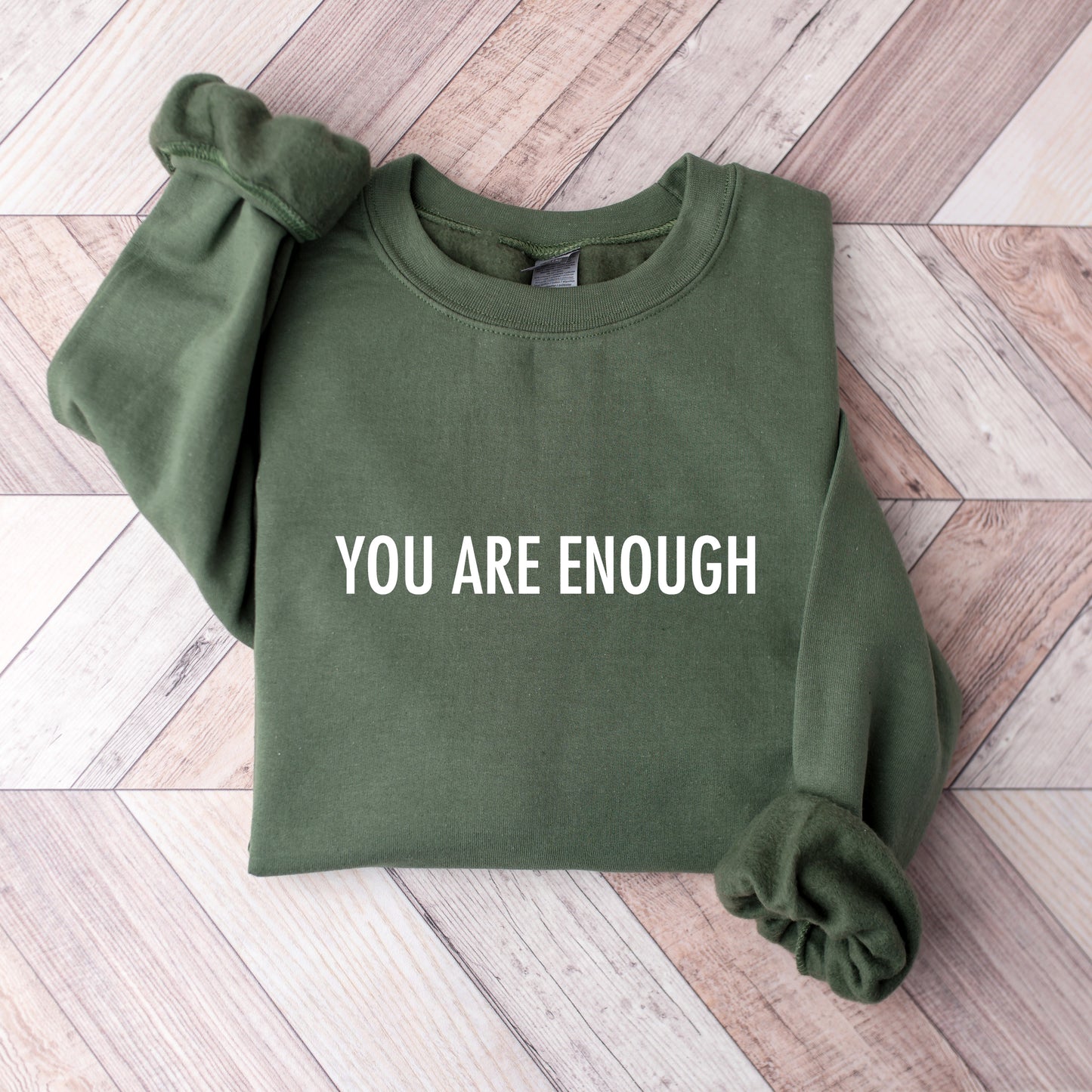 Green sweatshirt with You Are Enough Printed on it on a wooden floor