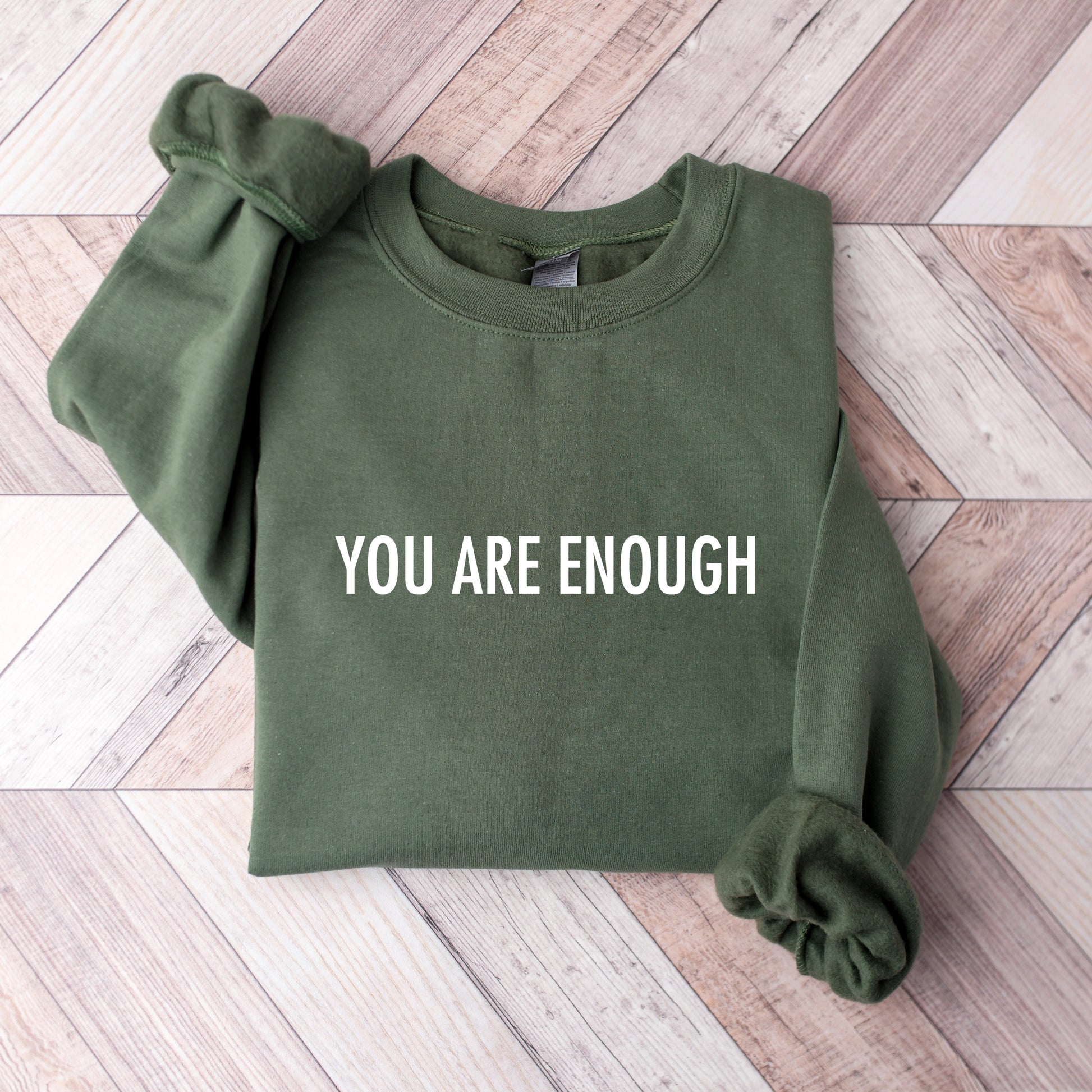Green sweatshirt with You Are Enough Printed on it on a wooden floor