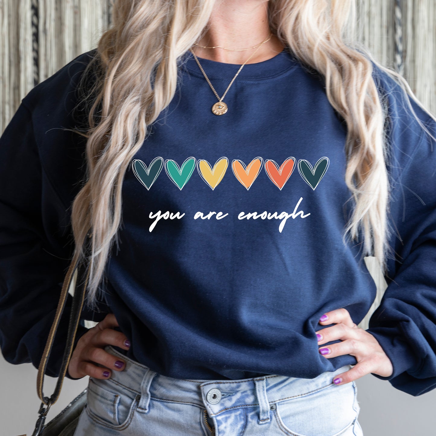 Person wearing a navy blue sweatshirt with colorful heart designs and 'you are enough' text.