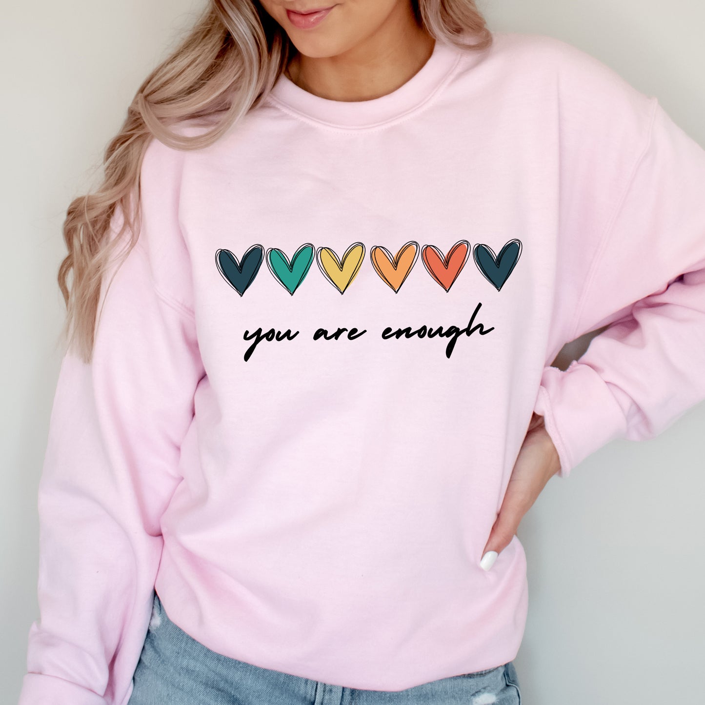 Person wearing a pink sweatshirt with colorful hearts and 'you are enough' text.