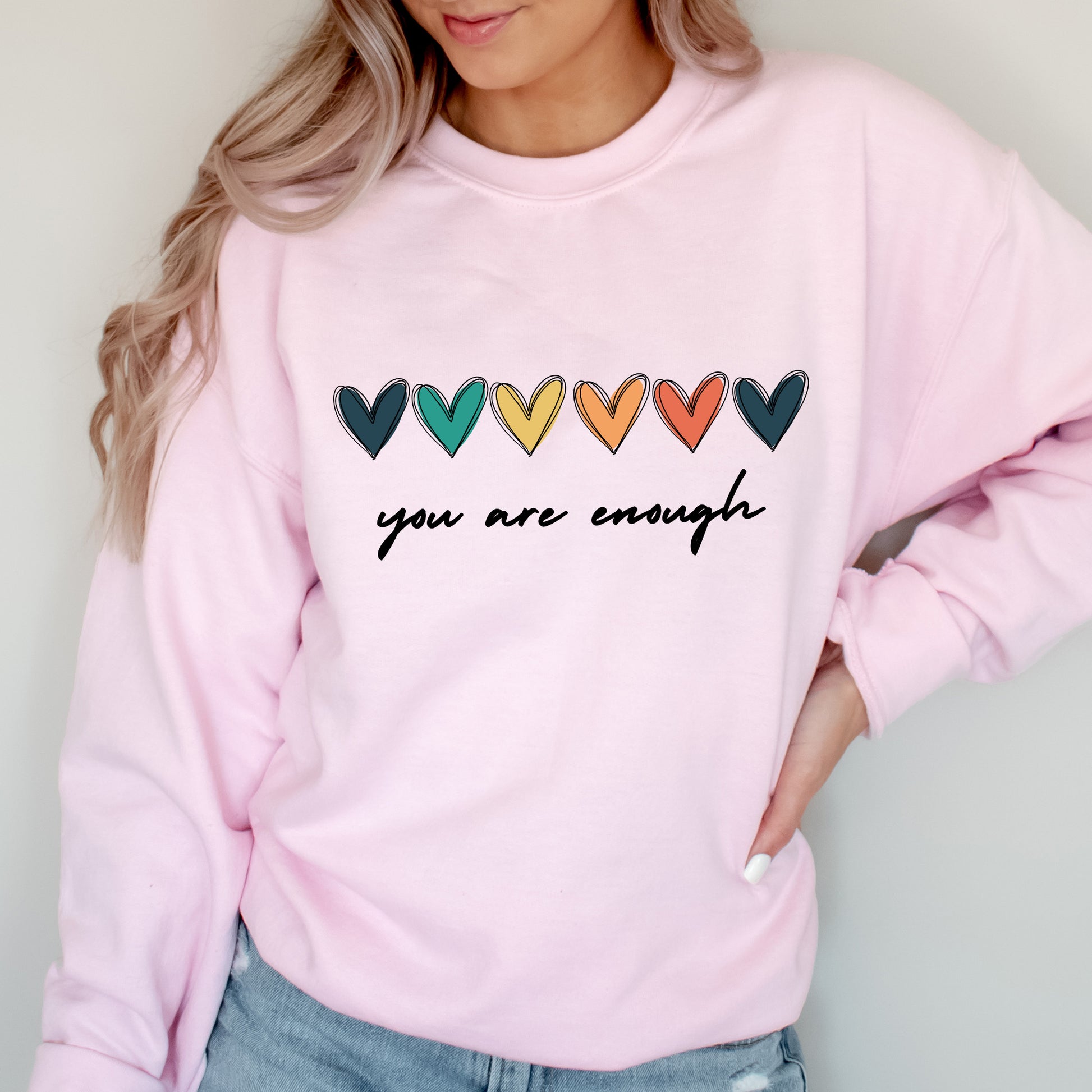 Person wearing a pink sweatshirt with colorful hearts and 'you are enough' text.