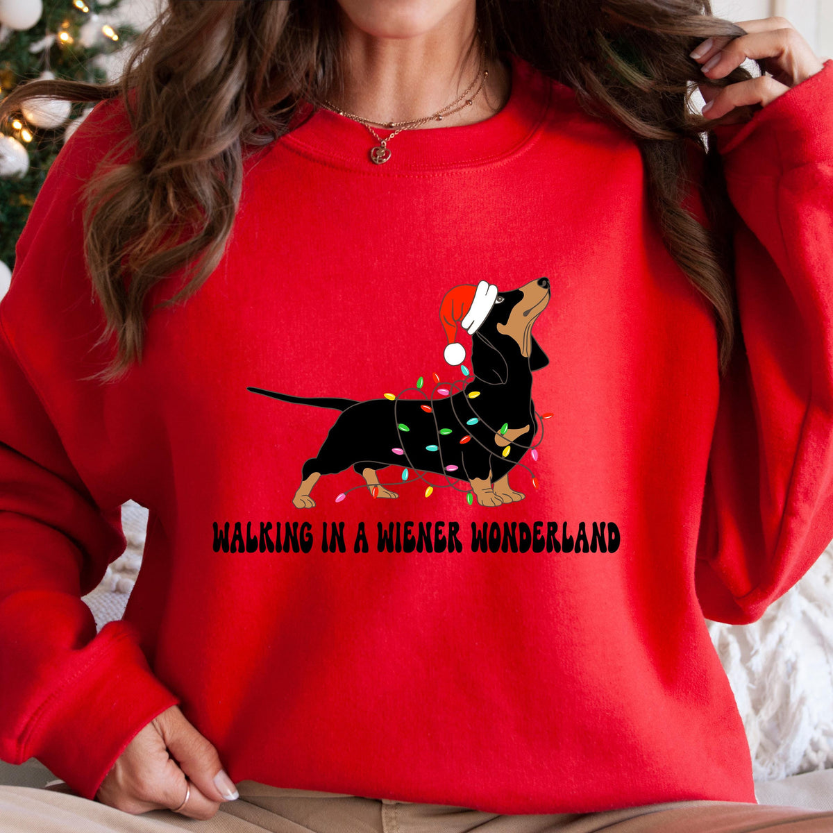 A red Gildan sweatshirt with a picture of a dachshund tangled in christmas lights and wearing a santa hat.  Beneath the picture are the words, Walking in a Wiener Wonderland