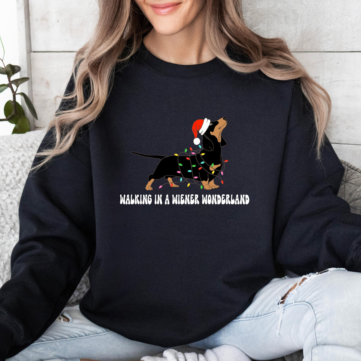 A black Gildan sweatshirt with a picture of a dachshund tangled in christmas lights and wearing a santa hat.  Beneath the picture are the words, Walking in a Wiener Wonderland